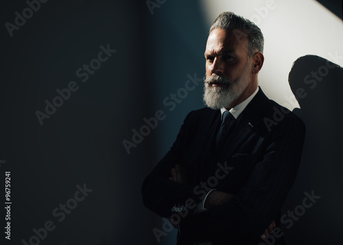 Portrait of stylish bearded man wearing trendy suit and stands against the wall. Horizontal