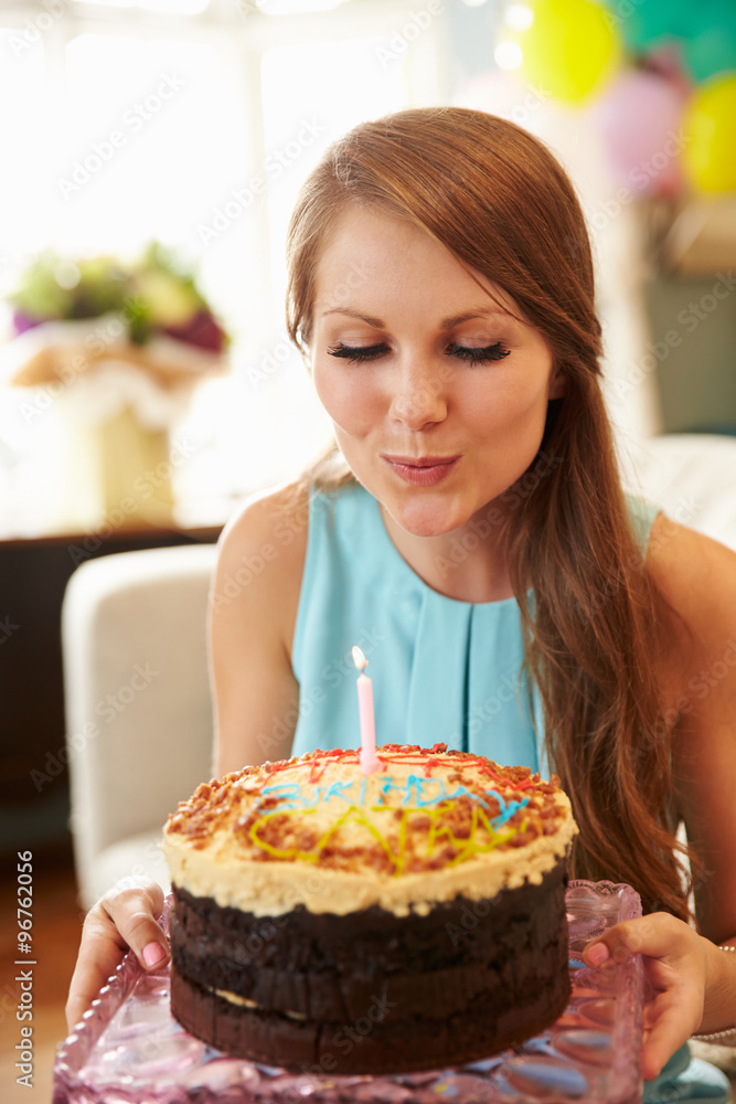 Young Woman Blowing Out Candle On Birthday Cake