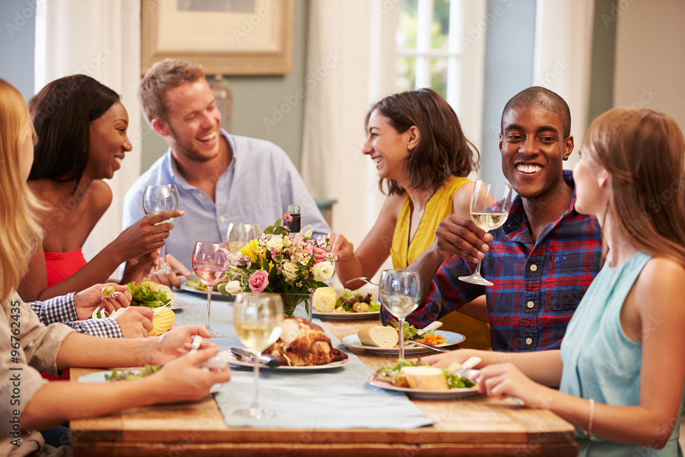Friends At Home Sitting Around Table For Dinner Party Friends At Home Sitting Around Table For Dinner Party