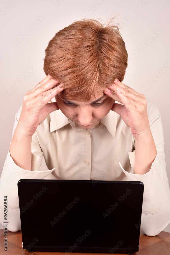 Worried businesswoman holding her head with hands and looking at the laptop Worried businesswoman holding her head with hands and looking at the laptop