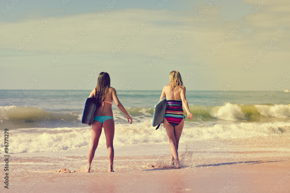 Back view of beautiful young women walking away with surfboards