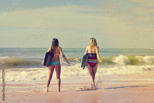 Back view of beautiful young women walking away with surfboards