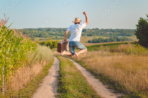 Backview of excited man with suitcase jumping on country road photo