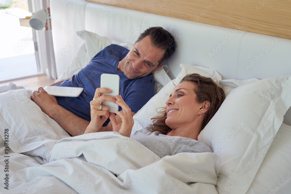 Obraz premium mature couple Using Digital Tablet And Mobile Phone In Bed At Ho