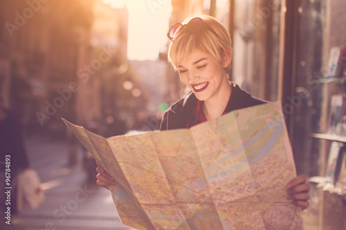 Young beautiful female traveler standing on the street and looking at the map photo