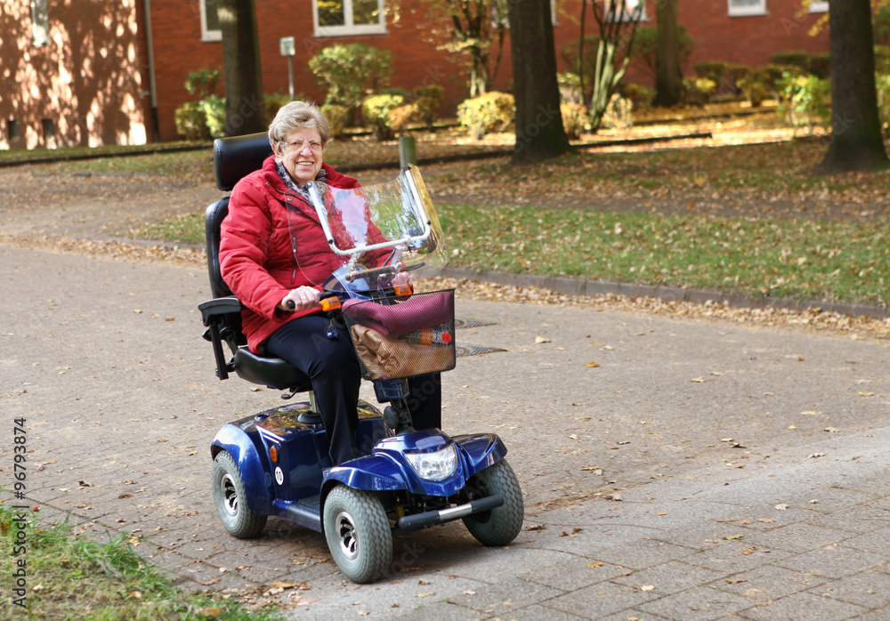 Seniorin mit Elektromobil fährt auf der Straße im Herbst Seniorin mit Elektromobil fährt auf der Straße im Herbst
