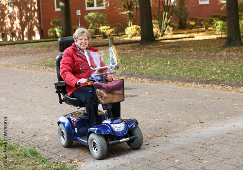 Seniorin mit Elektromobil fährt auf der Straße im Herbst