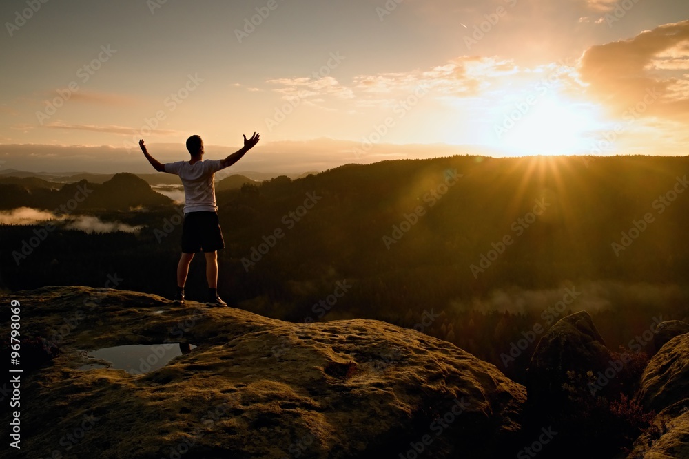 Runner on the peak. Man in his target gesture triumph with hands in the air. Crazy man in black pants and white cotton t-shirt,