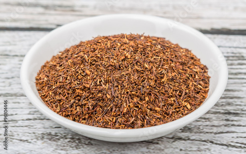 Dried South African rooibos herbal tea in white bowl over wooden background