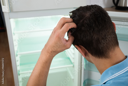 Confused Man Scratching Head While Looking At Empty Refrigerator