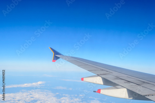 Wing of an airplane flying above the clouds and blue sky background