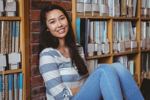 Smiling student sitting on the floor against wall in library