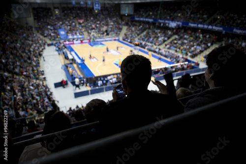 Fototapeta Divák na profesionální basketbalový zápas se podívá na svůj mobil během poločase