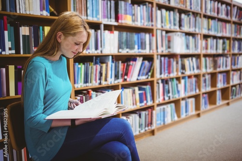 Smiling student sitting on chair reading book in library