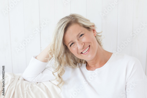 Obraz na płótnie beautiful adult woman with blond hair, smiling, happy drinking coffee, tea.He is sitting on the sofa with a cup in hand. w salonie