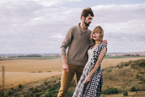 Loving couple wrapped in plaid standing on peak of mountain