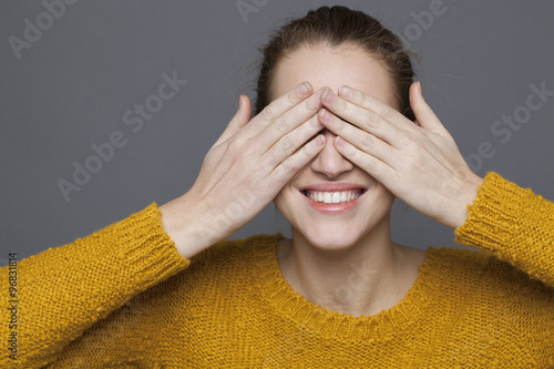 glowing happiness concept - playful 20s girl smiling in playing hide-and-seek for joy and serenity,studio shot on gray background