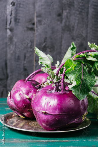 Kohlrabi cabbage with green leaves on a metal plate on wooden background of old vintage boards