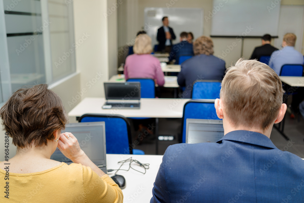 Informatics workshop at university. Rear view of students sitting and listening in lecture hall doing practical tasks on their laptops. Informatics workshop at university. Rear view of students sitting and listening in lecture hall doing practical tasks on their laptops.