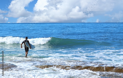 Canvas Print Surfer in black wet suit walking in to water on sunny day