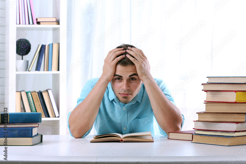 Young man reading book at table in room Young man reading book at table in room