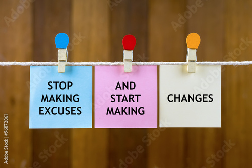 Word quotes of STOP MAKING EXCUSES AND START MAKING CHANGES on colorful sticky papers hanging by a rope against blurred wooden background. photo