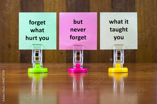 Word quotes of FORGET WHAT HURT YOU BUT NEVER FORGET WHAT IT TAUGHT YOU on colorful sticky papers against wooden textured background. photo