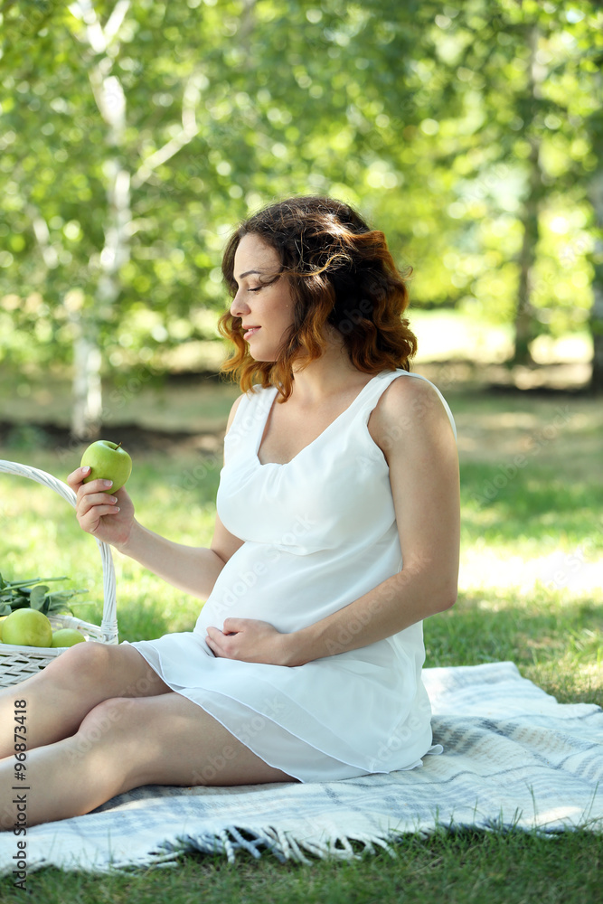 Attractive pregnant woman with apple on white blanket in the park