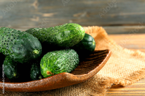 Fresh cucumbers in rustic bowl on wooden background