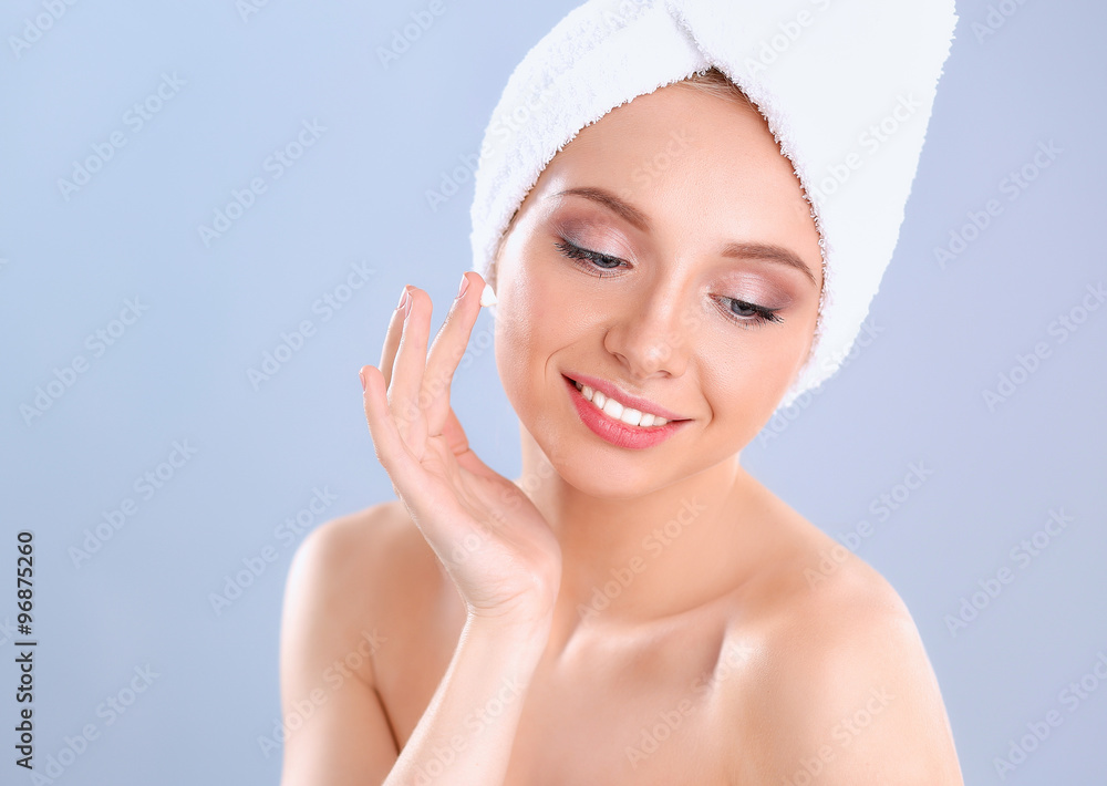 Beautiful young woman applying a creme on her face isolated on gray background Beautiful young woman applying a creme on her face isolated on gray background