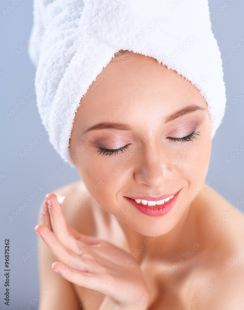Beautiful young woman applying a creme on her face isolated on gray background Beautiful young woman applying a creme on her face isolated on gray background