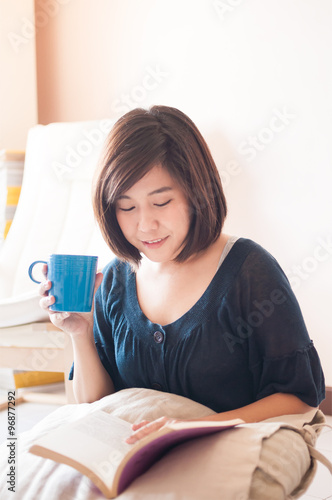 Young asian woman reading book and drinking coffee