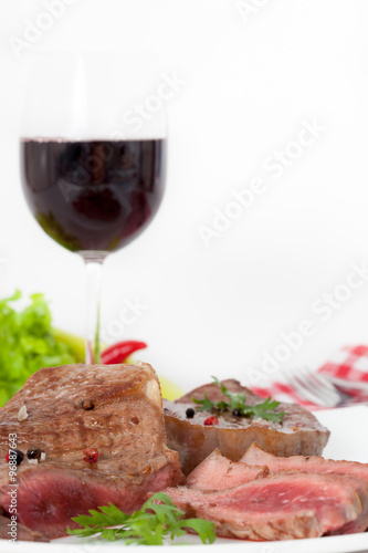 Beef steak on white plate with glass of red wine, vertical