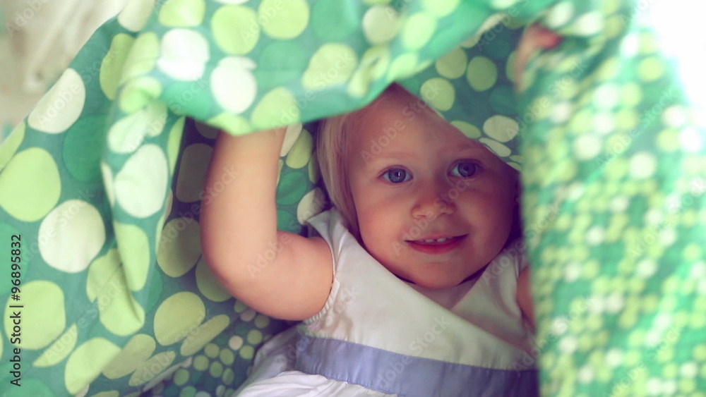 Cheerful baby girl playing hide and seek, cute playful child hiding under the covers, having fun
