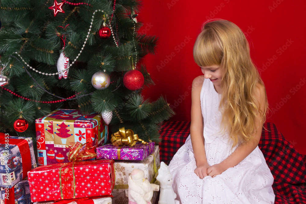 Beautiful baby girl sitting  near the Christmas tree in New Year's Eve smiling and holding a gift