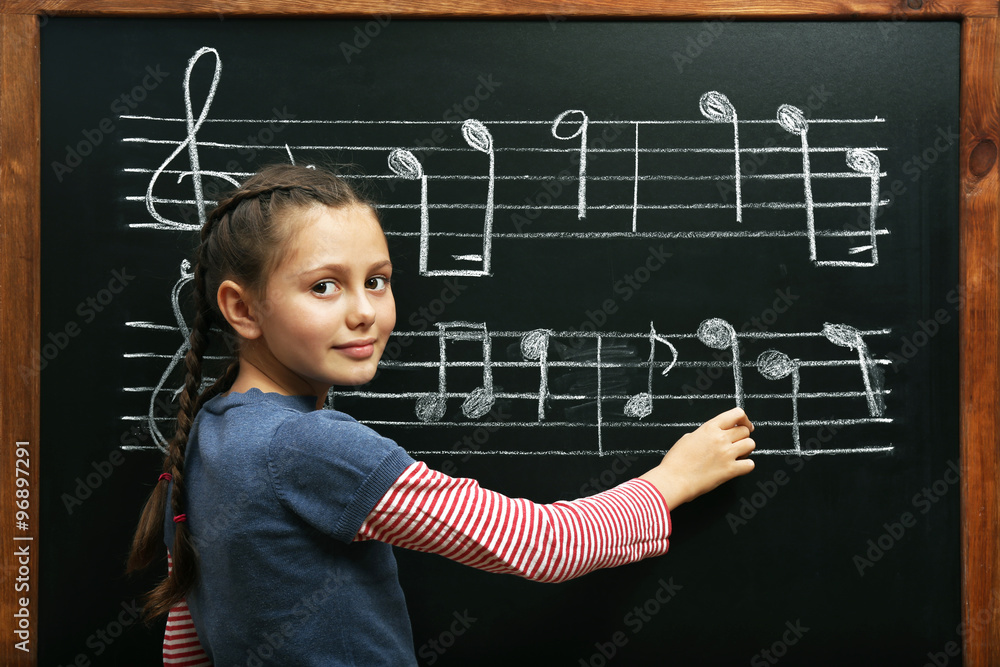 Cute girl writing at the blackboard with musical notes, in the classroom Cute girl writing at the blackboard with musical notes, in the classroom