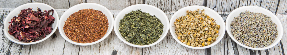 Dried herbal tea leaves, lavender, rooibos, chamomile, linden flower, hibiscus, Japanese green tea in white bowl over wooden background