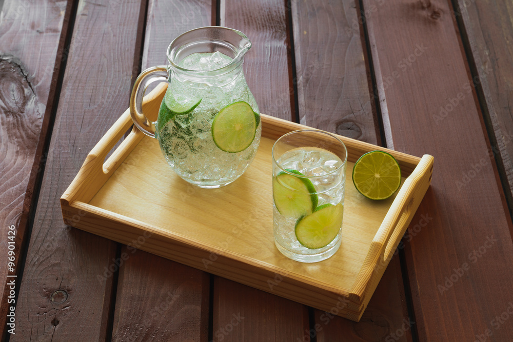 Drink and jug on wooden tray with ice and condensation on glass