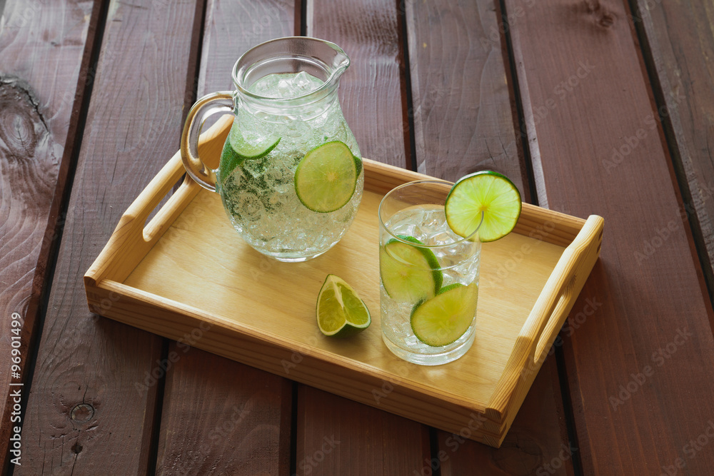 Drink and jug on wooden tray with ice and condensation on glass