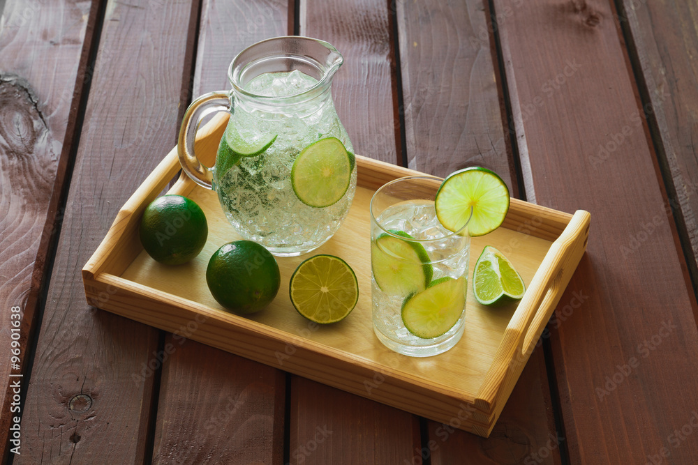 Drink and jug on wooden tray with ice and condensation on glass