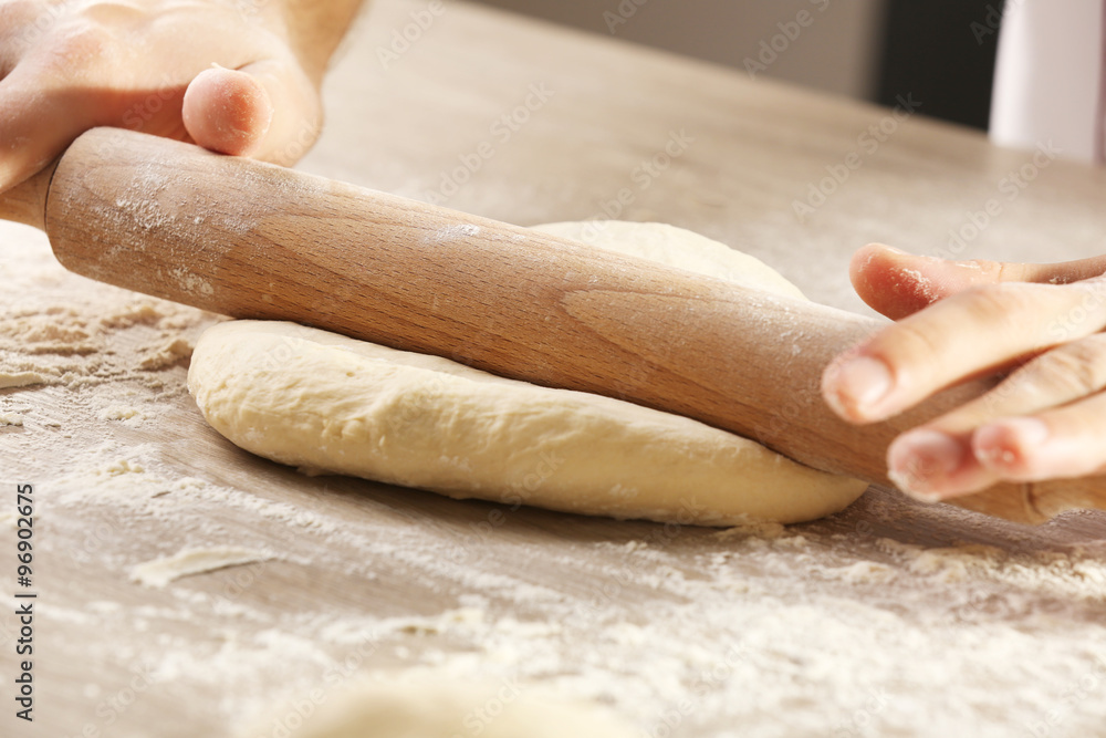 Hands rolling dough for pizza on the wooden table, close-up Hands rolling dough for pizza on the wooden table, close-up