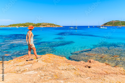 Young woman tourist standing on rock and looking at azure sea wa