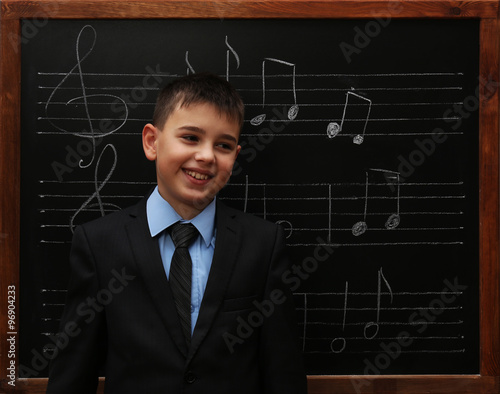 Young cute schoolboy standing at the blackboard with musical notes