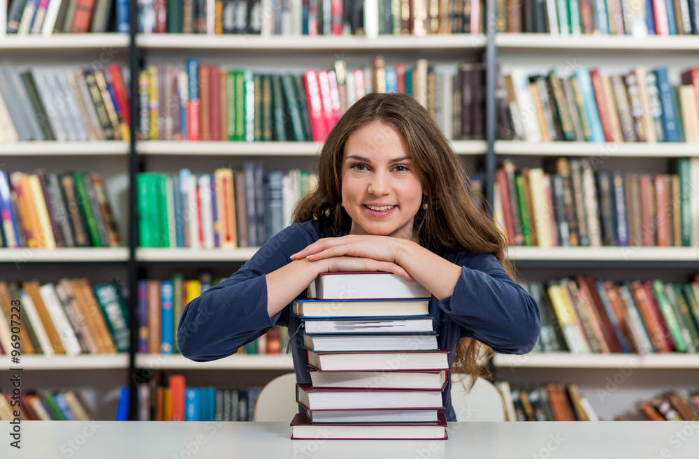 smiling young girl sitting at a desk in the library with her arm smiling young girl sitting at a desk in the library with her arm