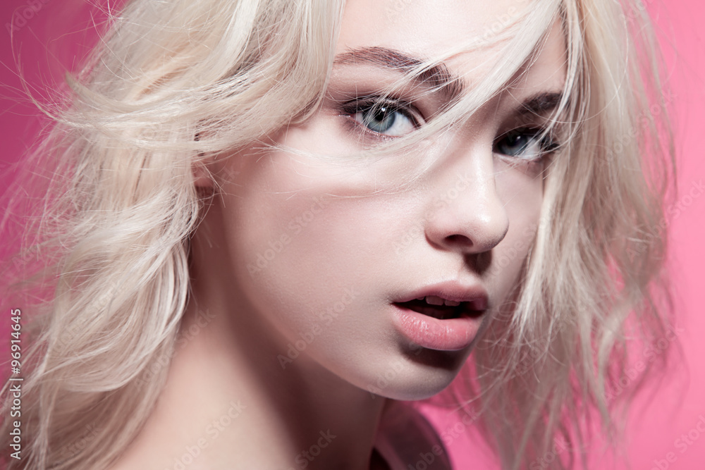 Obraz premium Close-up portrait of a woman with beautiful eyes and blonde hair on a pink background