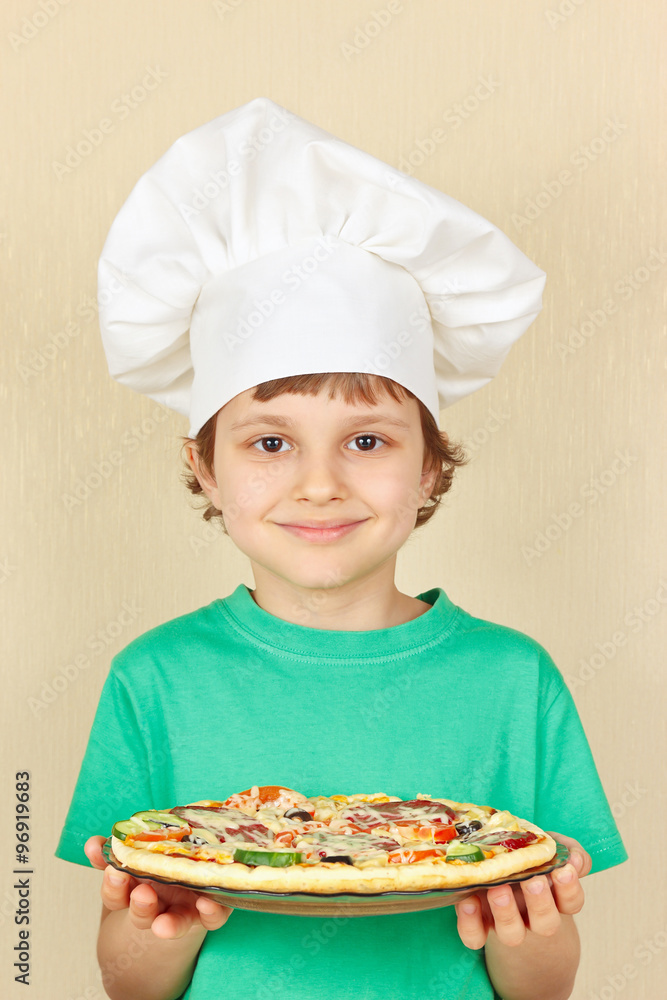Little boy in chefs hat with a cooked homemade pizza