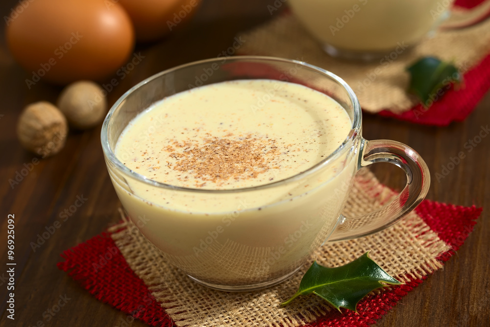Eggnog drink in glass cup sprinkled with ground nutmeg, photographed on dark wood with natural light (Selective Focus, Focus one third into the eggnog and on the handle of the cup) Eggnog drink in glass cup sprinkled with ground nutmeg, photographed on dark wood with natural light (Selective Focus, Focus one third into the eggnog and on the handle of the cup)