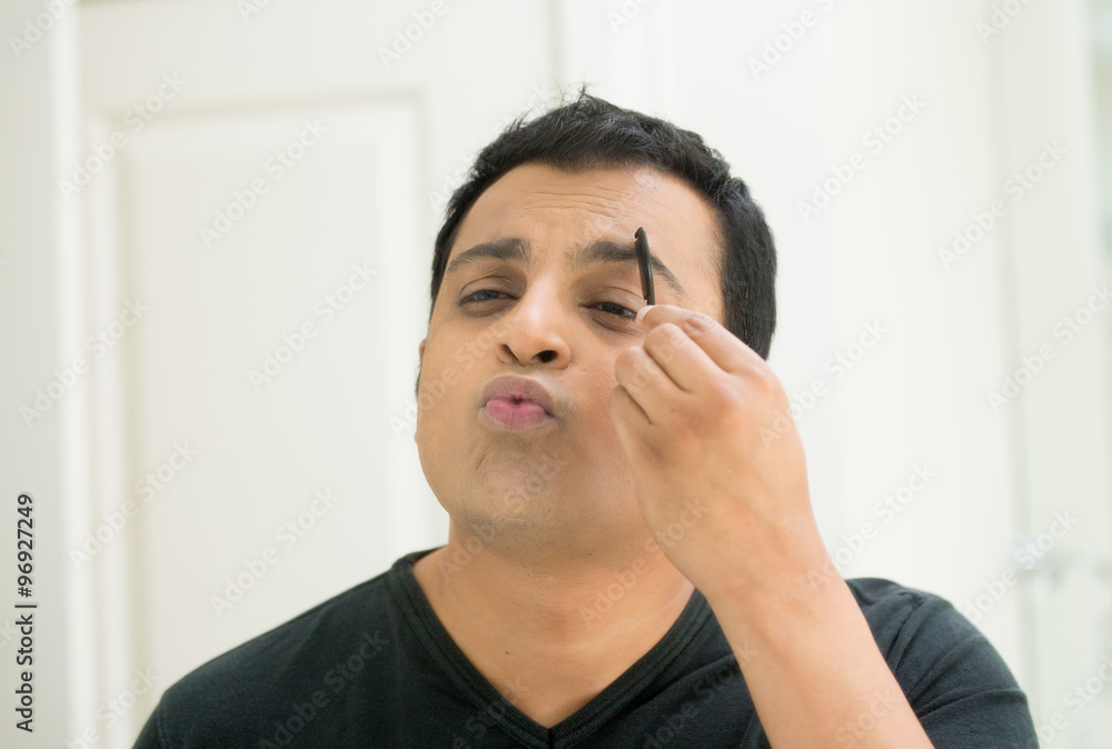 Closeup portrait, young handsome egotistical man in black t-shirt looking at mirror showing kisses and duck face, combing eyebrows admiring his appearance inside indoors background Closeup portrait, young handsome egotistical man in black t-shirt looking at mirror showing kisses and duck face, combing eyebrows admiring his appearance inside indoors background