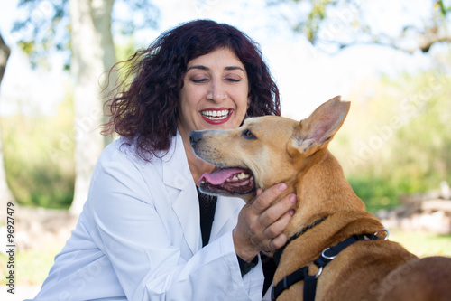 Closeup portrait, sweet moments healthcare professional in white lab coat with dog, checking lymph nodes, isolated sunny outdoors outside background, green trees