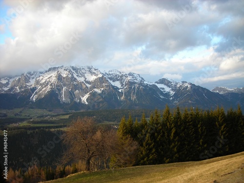 Panoramic view on the early spring landscape in the mountains featuring green hills and snow covered mountain tops in the distance. Austrian Alps, ski resort Schladming.
